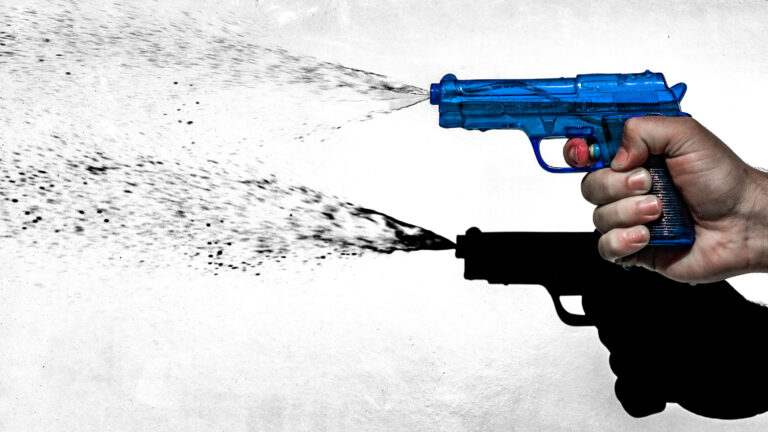 Hand holding a blue toy water gun spraying water to the left against a white background.