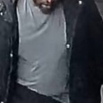 Bearded man in a gray shirt and dark jacket looking down, as if focused or thinking.