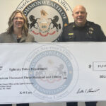 Two officials hold a large ceremonial check for the Ephrata Police Department K-9 Unit, $19,315.77, with a district seal in the background.