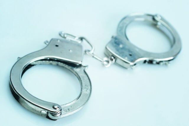 Pair of silver handcuffs resting on a pale blue surface, linked together by a chain