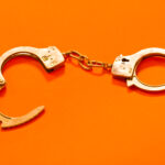 Two metal handcuffs connected by a short chain on a bright orange background; one cuff is open.