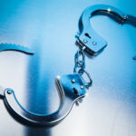 Pair of metal handcuffs linked by a chain on a blue reflective surface.