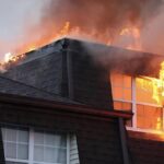 House on fire with flames and smoke engulfing the roof and a second-story window area.