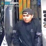 Surveillance image of a man in a black jacket and backward cap inside a store; Crime Stoppers overlay with phone number 800-577-8477 visible.