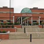 Front of Howell Township Municipal Building with brick facade, glass arch, and stepped entrance with metal rails; landscaping on either side.