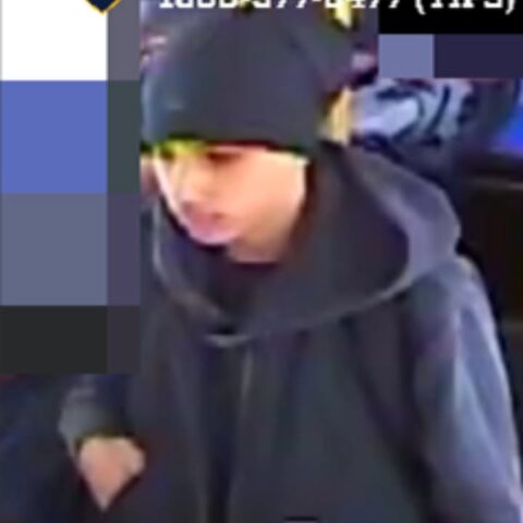 Person wearing a dark hoodie and beanie, looking down in a dim indoor setting; partial colored pixelation on the left side of the frame.