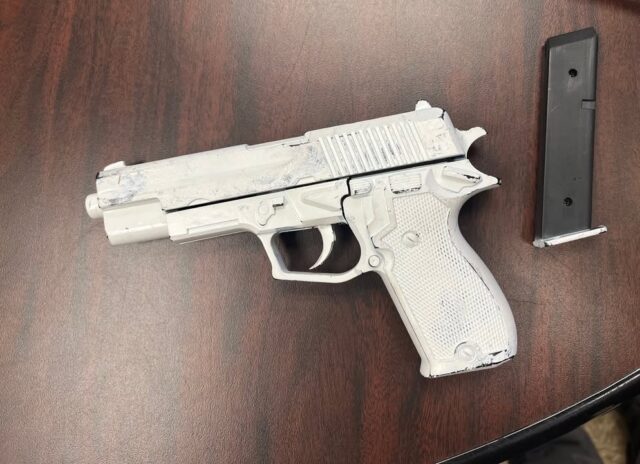 Semi-automatic pistol with a gray finish on a wooden table, with its magazine lying nearby.