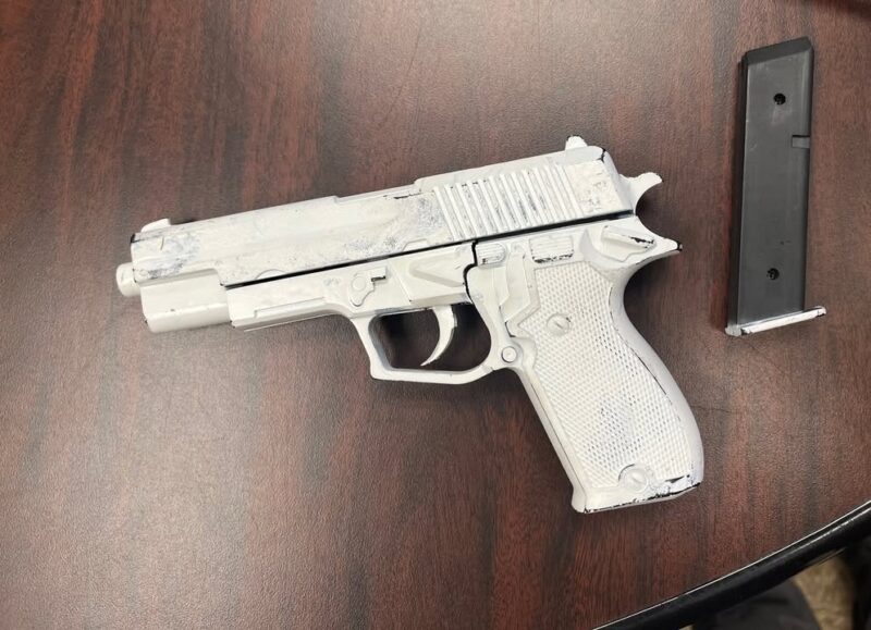 Semi-automatic pistol with a gray finish on a wooden table, with its magazine lying nearby.