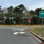 Intersection scene: STOP painted on the road with a curved right-turn arrow, crossing into a divided street with yellow bollards and a Beaverson Blvd West sign on the right.