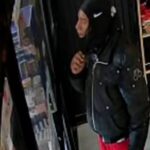Surveillance image of a man in a black hooded jacket and red pants inside a store; Crime Stoppers logo in the corner.