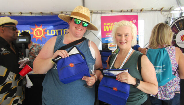 Two attendees at a maryland lottery booth pose for a photo, each holding a blue prize bag and smiling at the camera with drinks in hand.