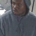 Man wearing a gray hoodie indoors, looking downward.