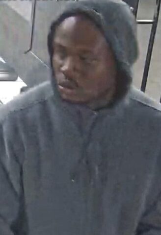 Man wearing a gray hoodie indoors, looking downward.
