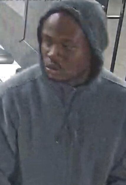 Man wearing a gray hoodie indoors, looking downward.