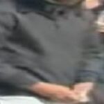Hooded man in a black jacket stands beside a car with hands cuffed behind his back; Crime Stoppers banner visible in the top corner.