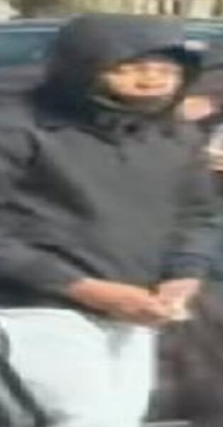 Hooded man in a black jacket stands beside a car with hands cuffed behind his back; crime stoppers banner visible in the top corner.