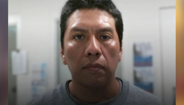 Close-up portrait of a man with short black hair in a gray shirt, looking at the camera in a plain indoor setting.