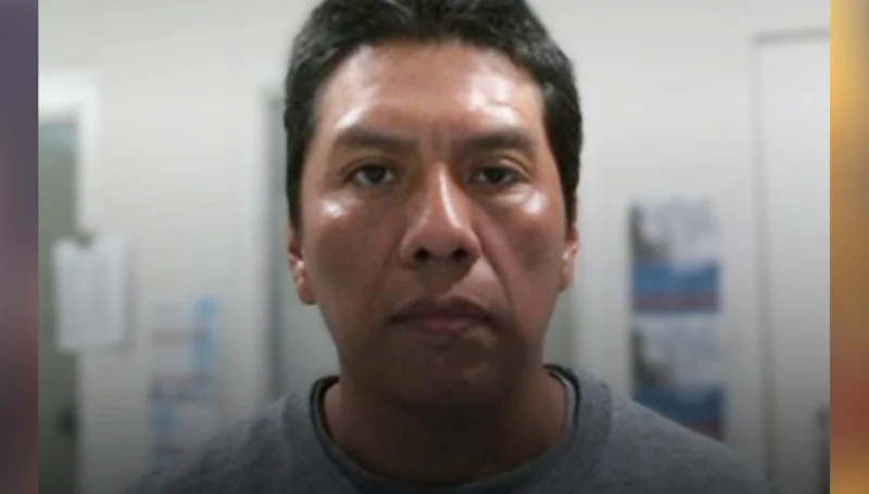 Close-up portrait of a man with short black hair in a gray shirt, looking at the camera in a plain indoor setting.