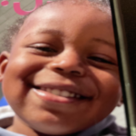 Close-up of a smiling young child facing the camera with dimples and showing teeth