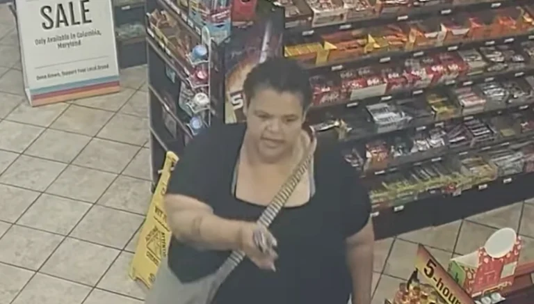 Surveillance image of an adult woman in a black top with a striped crossbody bag, standing in a store aisle near snack shelves.