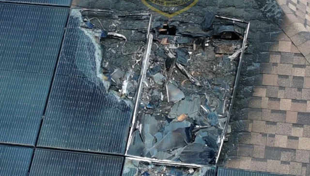 Damaged solar panel array with shattered glass and exposed interior components on a rooftop.