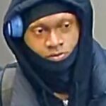 Close-up of a person wearing a dark hoodie and scarf, with a blue headset over one ear, looking to the left.