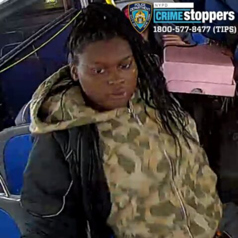 Young woman with long braids wearing a camo jacket and dark hoodie sits on a bus; crime stoppers logo in the top-right corner.