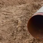 Large corrugated metal pipe lying in a dirt trench, ready for installation at a construction site.