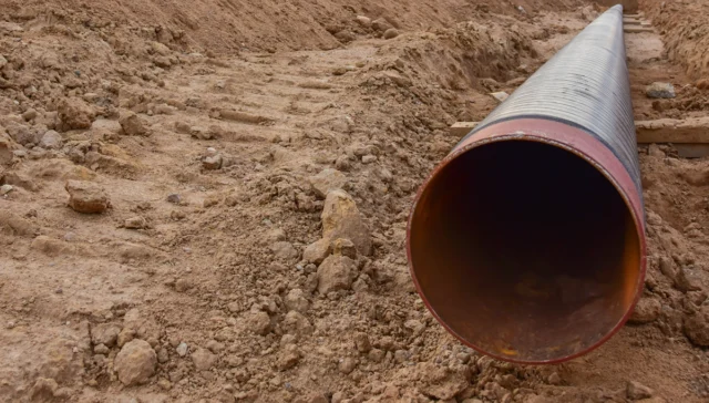 Large corrugated metal pipe lying in a dirt trench, ready for installation at a construction site.