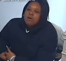 Woman in a black hoodie sitting on a sofa, looking surprised off-camera.