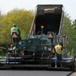 Road Paving. Paving a residential street by laying asphalt which is initially in the dump truck and then is 'pressed' down to form the new road surface.