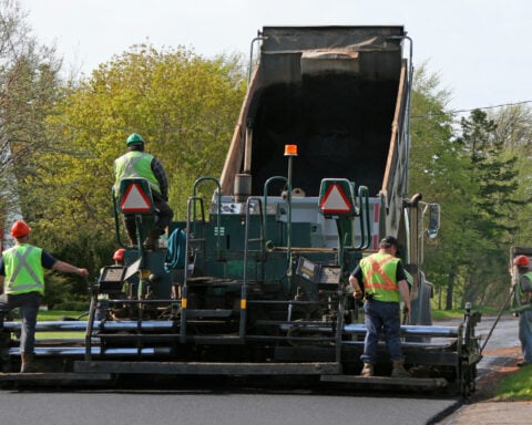 Road Paving. Paving a residential street by laying asphalt which is initially in the dump truck and then is 'pressed' down to form the new road surface.