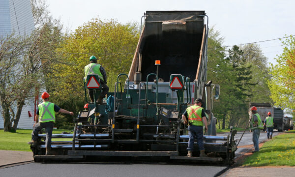 Road Paving. Paving a residential street by laying asphalt which is initially in the dump truck and then is 'pressed' down to form the new road surface.