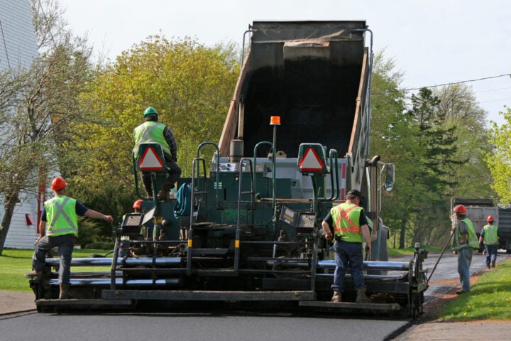 Road Paving. Paving a residential street by laying asphalt which is initially in the dump truck and then is 'pressed' down to form the new road surface.