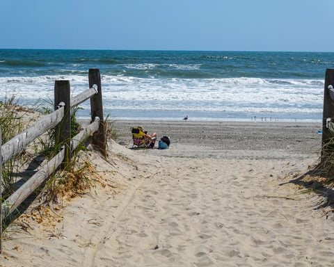 Ventnor, New Jersey - Fall - View along a sand path with a wooden fence towards an empty beach with one girl sunbather siting on a chair. Photo by Alan Budman