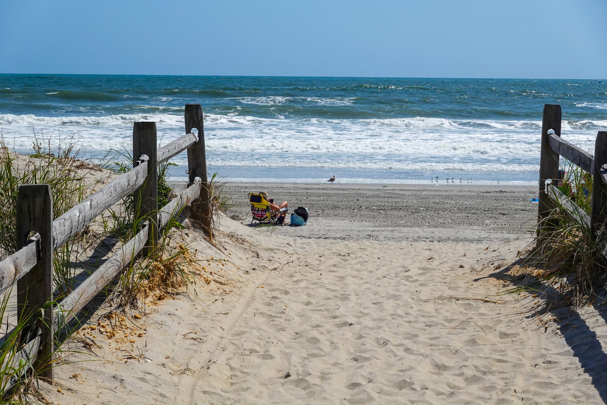 Ventnor, new jersey - fall - view along a sand path with a wooden fence towards an empty beach with one girl sunbather siting on a chair. Photo by alan budman